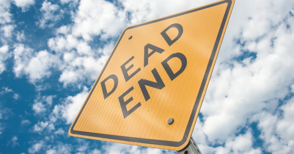 Close-up of a dead end road sign against a bright, cloudy blue sky, symbolizing restriction and caution.