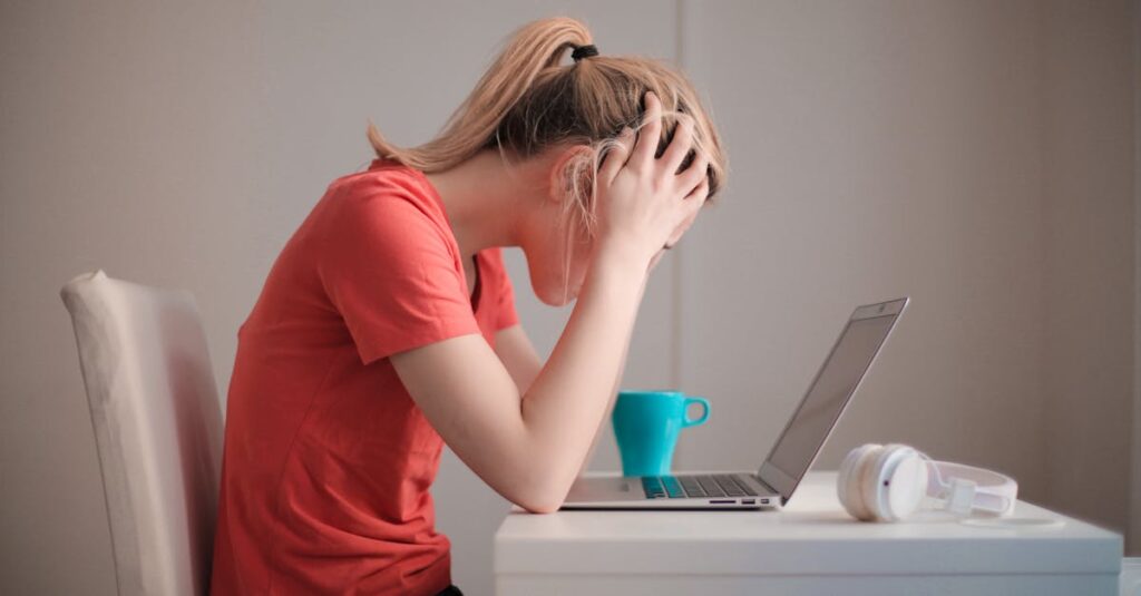 Young woman feeling stressed while studying at home with a laptop and coffee cup.