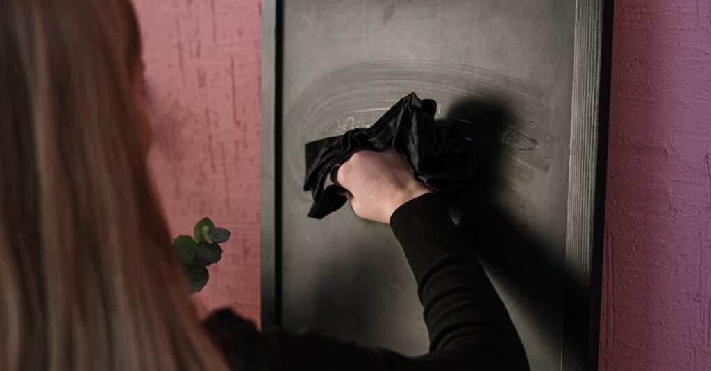 A woman using a cloth to erase a black chalkboard in an indoor setting.