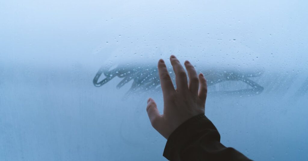 A hand touches a foggy glass window, creating a misty atmosphere outdoors.