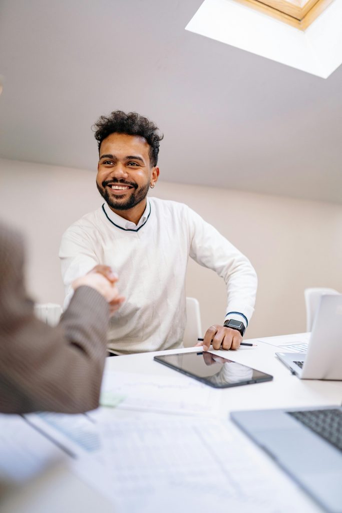 pexels-photo-7693151-7693151 A smiling man in business attire shakes hands across a desk in a modern office.